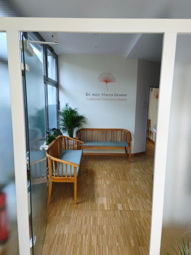 Wartebereich mit Holzbank, Pflanze und Wandtafel in hellen Farben.